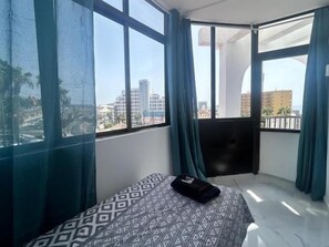 A room with a bed, a TV, and a balcony with curtains.