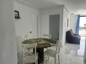 Un coin repas avec une table en marbre et des chaises blanches, un balcon avec un canapé et une vue sur la mer.