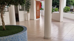 A spacious indoor area with tiled flooring, a circular blue-tiled planter with grass, and white pillars. - Garajonay 3 bedrooms apartment, ocean pool view (Costa de Adeje)