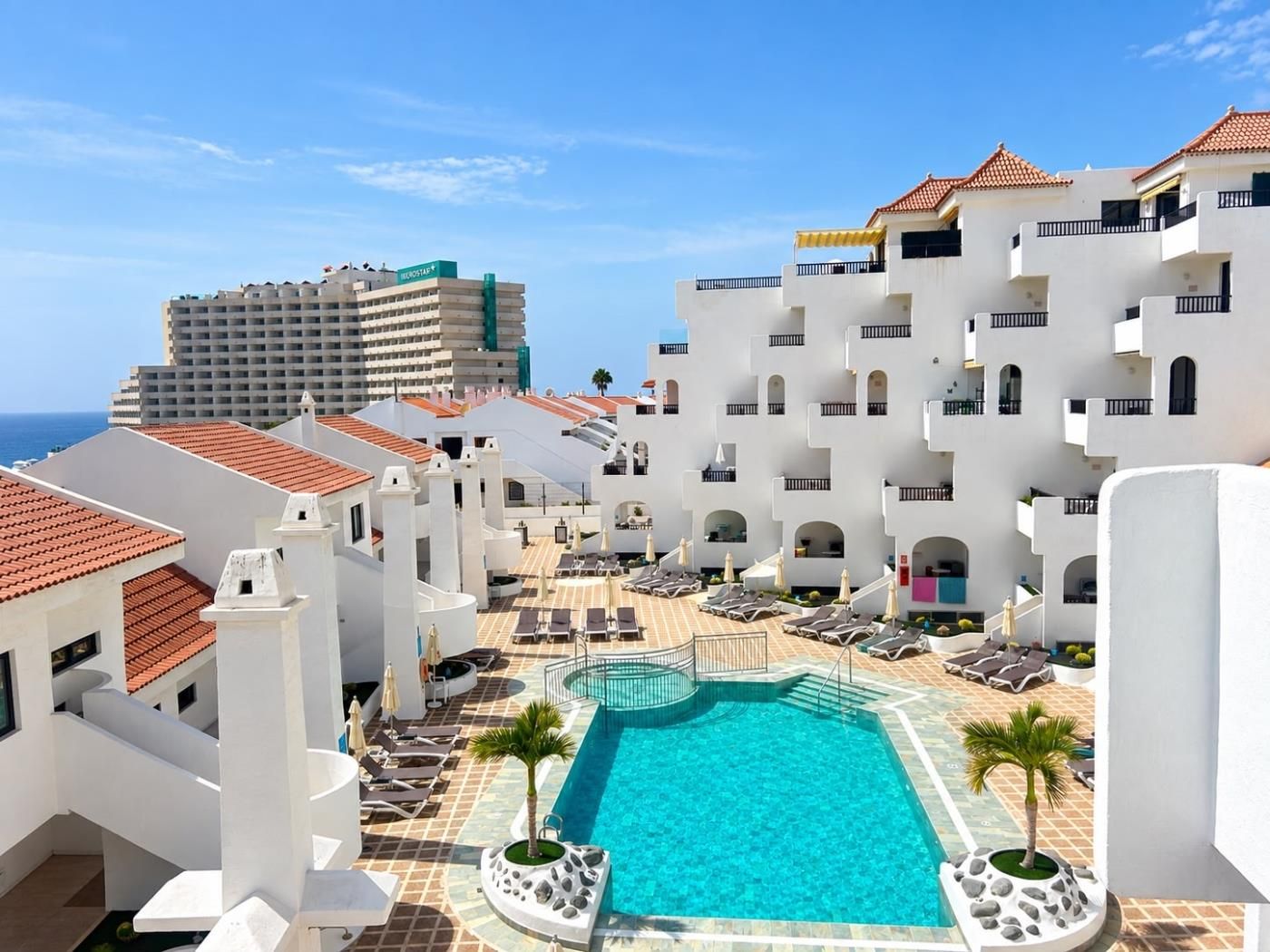 A resort with a swimming pool surrounded by lounge chairs and palm trees.