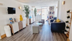 A modern living room with a sofa, coffee table, and a TV mounted on the wall. There are plants and a small dining area visible. - Garajonay 3 bedrooms apartment, ocean pool view (Costa de Adeje)