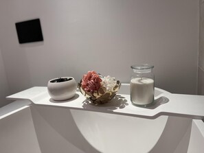 A white table with a small white bowl, a glass jar with a candle, and a decorative arrangement of flowers and leaves. - Immaculate 2-bed Apartment in London (London)