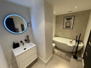 A modern bathroom with a round mirror, white vanity, and a freestanding bathtub. - Immaculate 2-bed Apartment in London (London)
