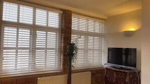 A living room with large windows, a radiator, a TV, and a wooden cabinet. - Immaculate 2-bed Apartment in London (London)