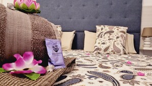 Una cama bien hecha con ropa de cama estampada, una almohada decorativa, una toalla enrollada y una pequeña bolsa con la etiqueta 'HOLIDAYS Tenerife'.