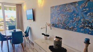 Una habitación moderna con zona de comedor, televisor montado en la pared y un cuadro grande con motivos florales.