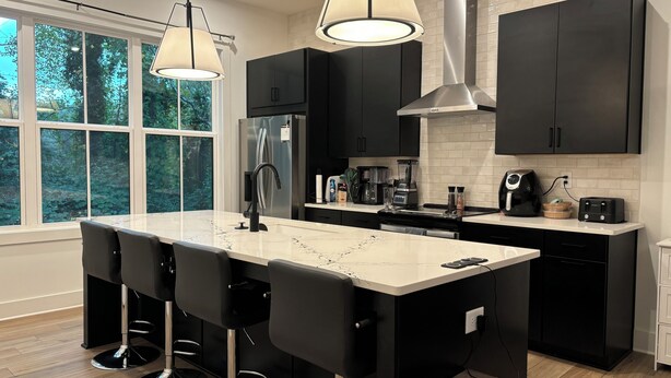 A modern kitchen with a central island, black cabinetry, stainless steel appliances, and pendant lighting.