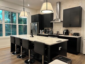 A modern kitchen with a central island, black cabinetry, stainless steel appliances, and pendant lighting. - Executive level Grant Park, Chosewood Park, Atlanta 3 Story Townhome w/ Garage
 (Atlanta)