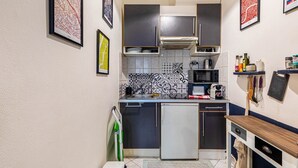 Ett kompakt kök med moderna apparater, en mikrovågsugn, en brödrost och ett litet kylskåp. Det finns dekorativa kakelplattor på väggen bakom arbetsbänken och några inramade tavlor på väggen.