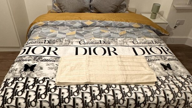 A bed with a bedspread featuring the Christian Dior logo and the words "Exclusive Edition" on it. - 6-bed 3-bath Home - Sleeps 14 & Free Parking (Uxbridge)