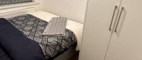 A small bedroom with a bed, a wardrobe, and a window with blinds.
