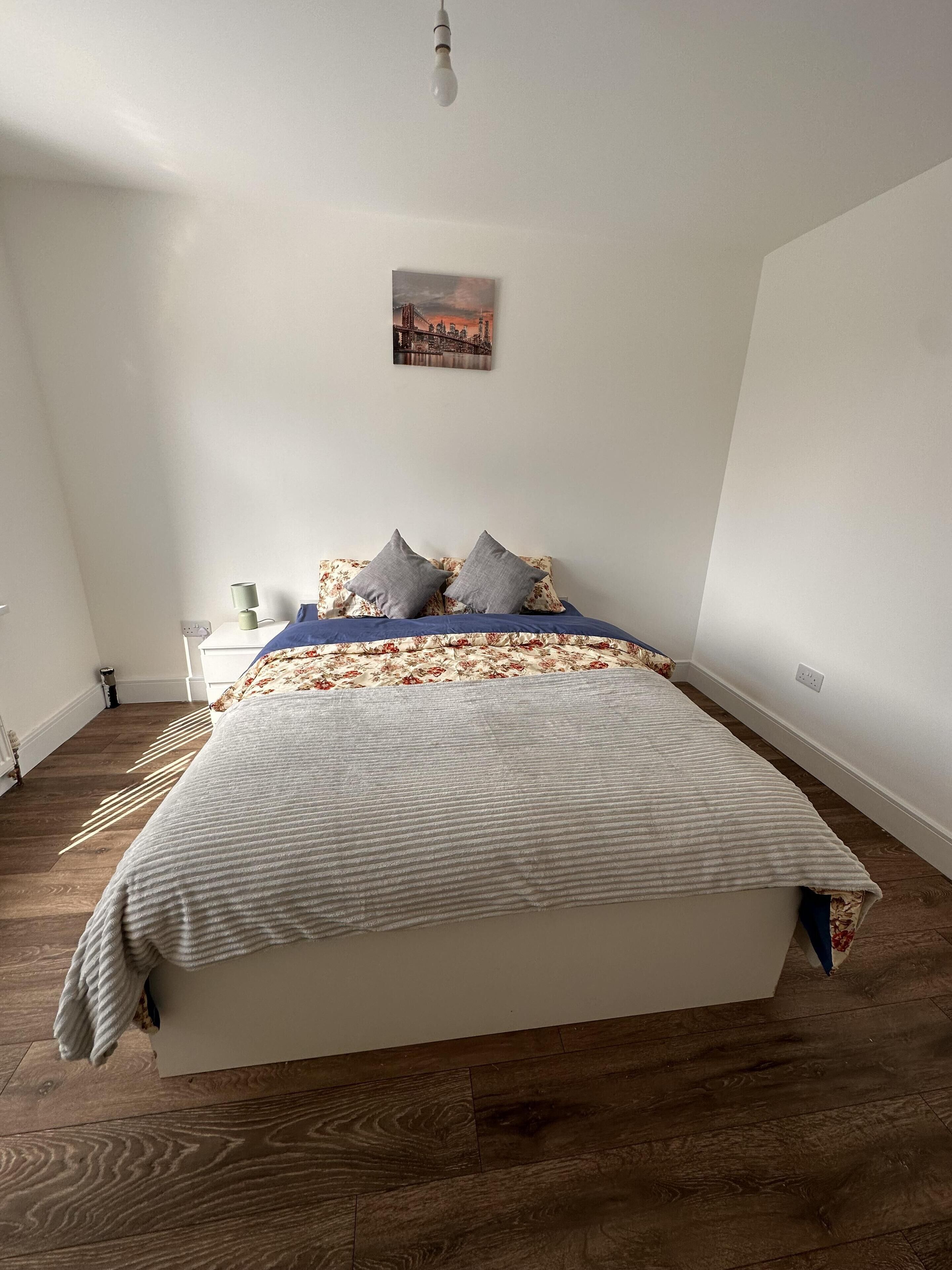 A bedroom with a bed, a nightstand, a lamp, and a wall-mounted picture.
