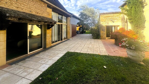 A courtyard with a paved walkway, a grassy area, and a building with large windows and a stone facade.