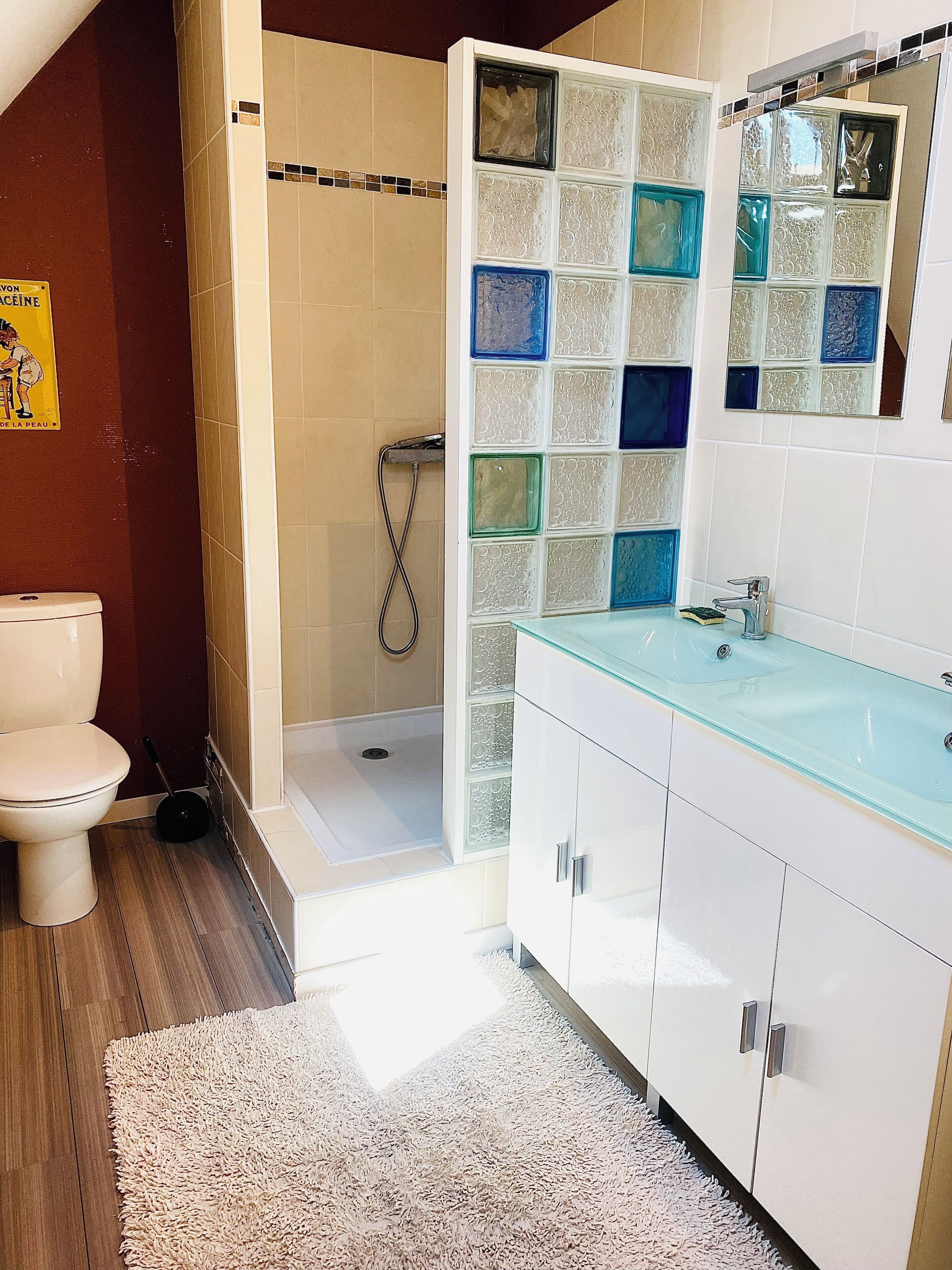 A bathroom with a glass shower enclosure, a white toilet, and a glass sink with a white cabinet.