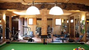 A room with a pool table, exercise equipment, and a brick pillar.