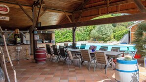 Een terras buiten met houten tafels en stoelen, een zwembad en een cafégedeelte.