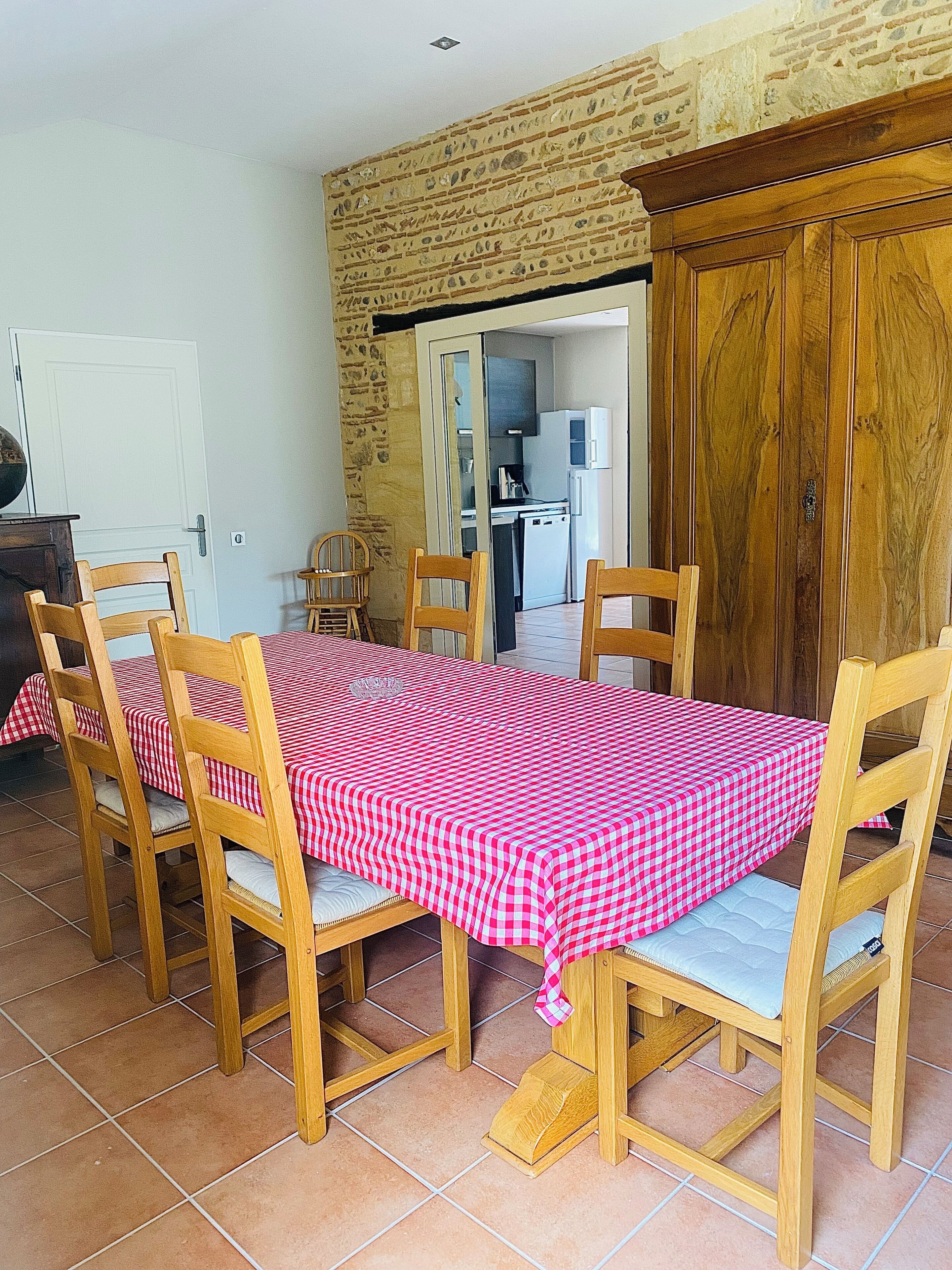 Un coin repas avec une nappe à carreaux, des chaises en bois et une cuisine en arrière-plan.