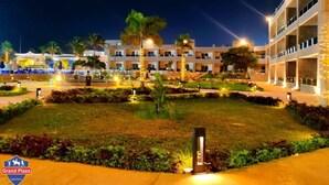 A hotel with multiple floors, a well-lit courtyard, and palm trees. - Grand Plaza Hotel (Kirdasah)