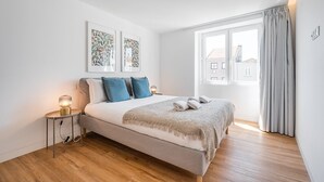 Een moderne slaapkamer met een bed, een nachtkastje met een lamp, en twee ingelijste botanische prints aan de muur.