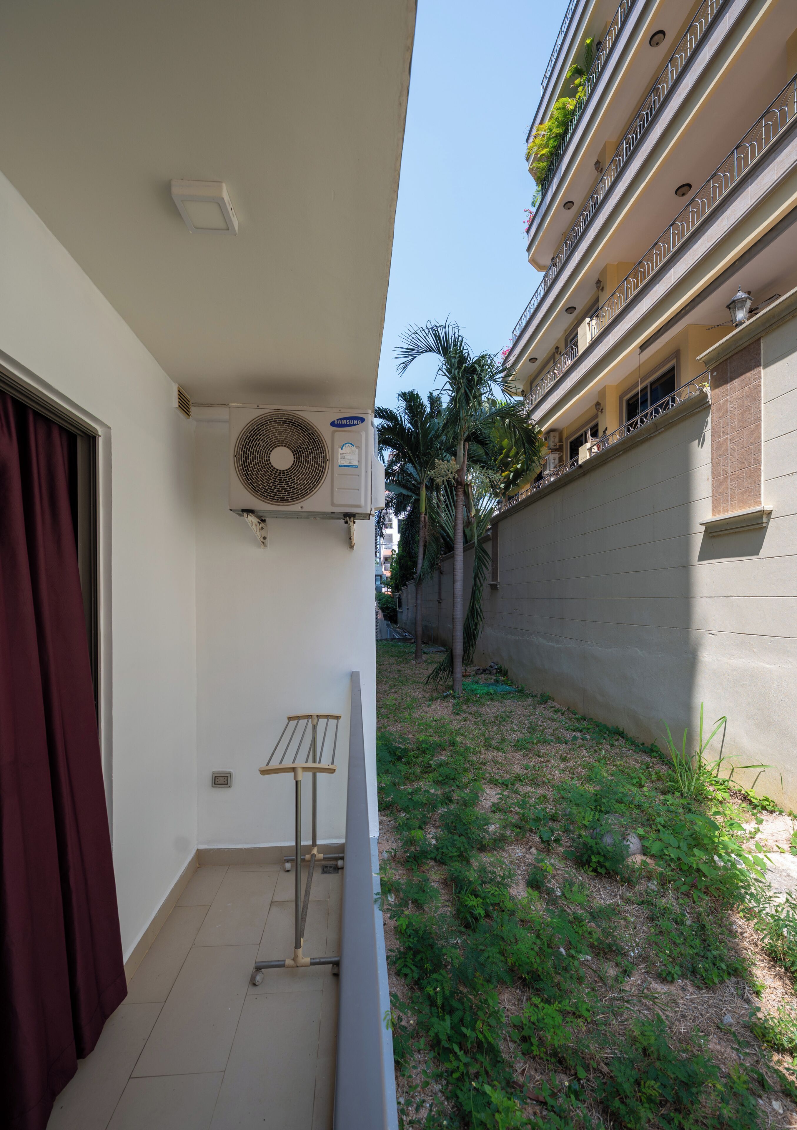 A balcony with a Samsung air conditioner, a small table, and a view of a neighboring building with balconies.