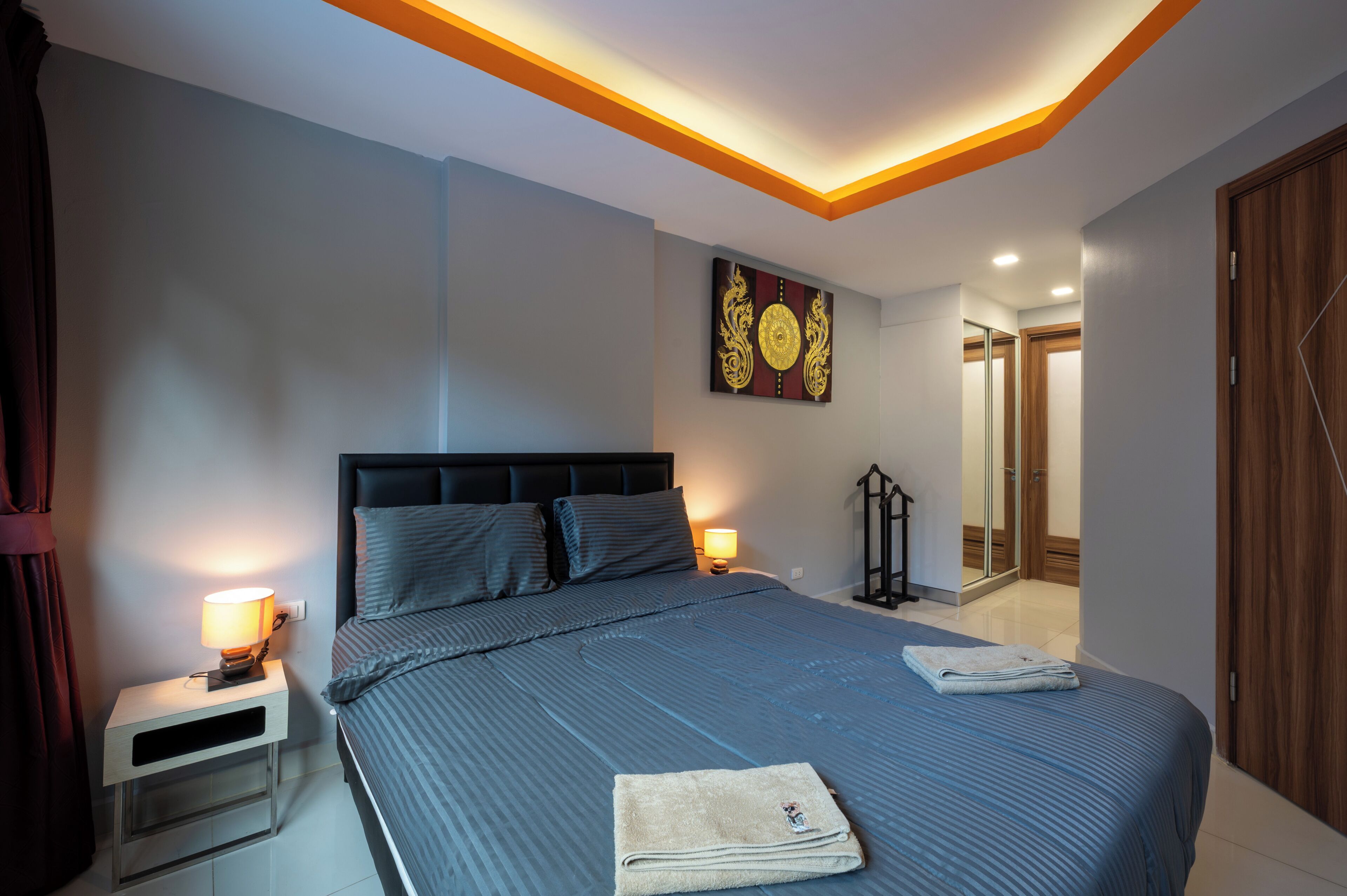 A bedroom with a bed, bedside lamps, a nightstand, a wall-mounted artwork, and a door.