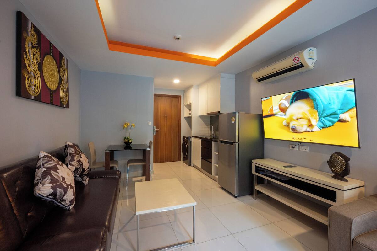 Een moderne woonkamer met een bank, een salontafel, een televisie en een keukenhoek met een koelkast en magnetron.