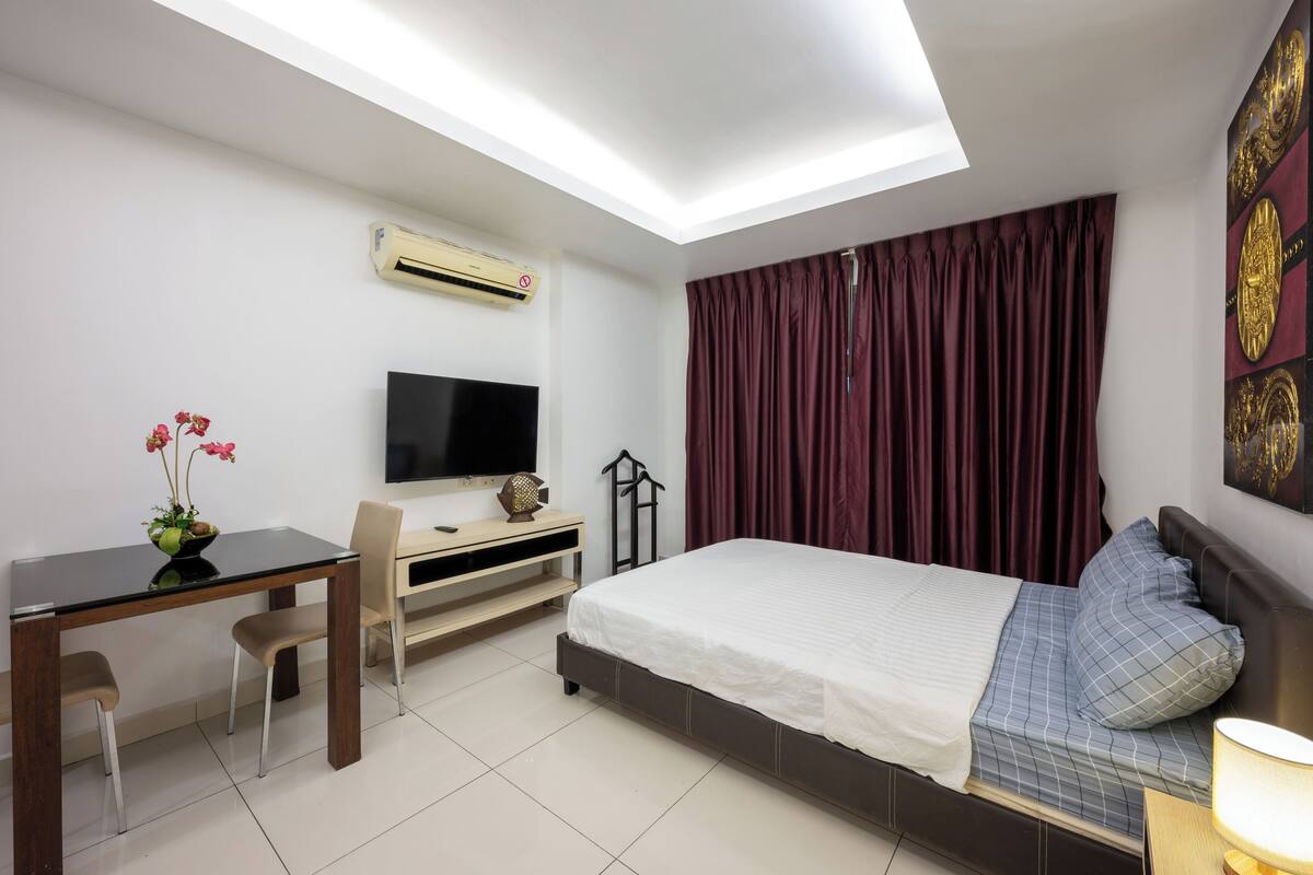 Een hotelkamer met een bed, een bureau met stoel, een televisie en een raam met gordijnen.