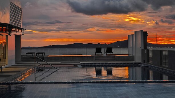 Una piscina en la azotea con vistas al atardecer, un edificio con un ventanal grande y una barandilla de metal.