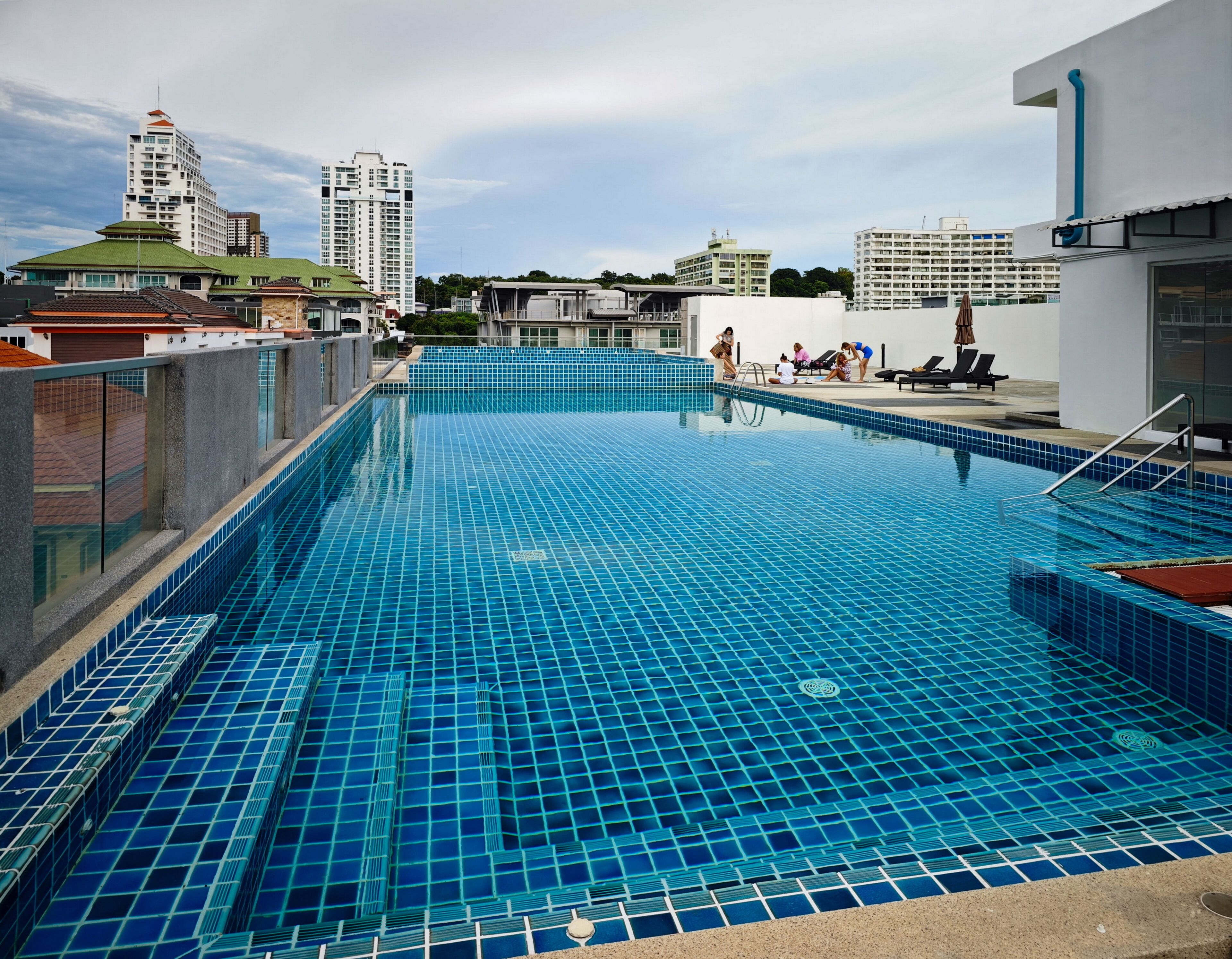 A rooftop pool with blue tiles, surrounded by buildings and a clear sky.