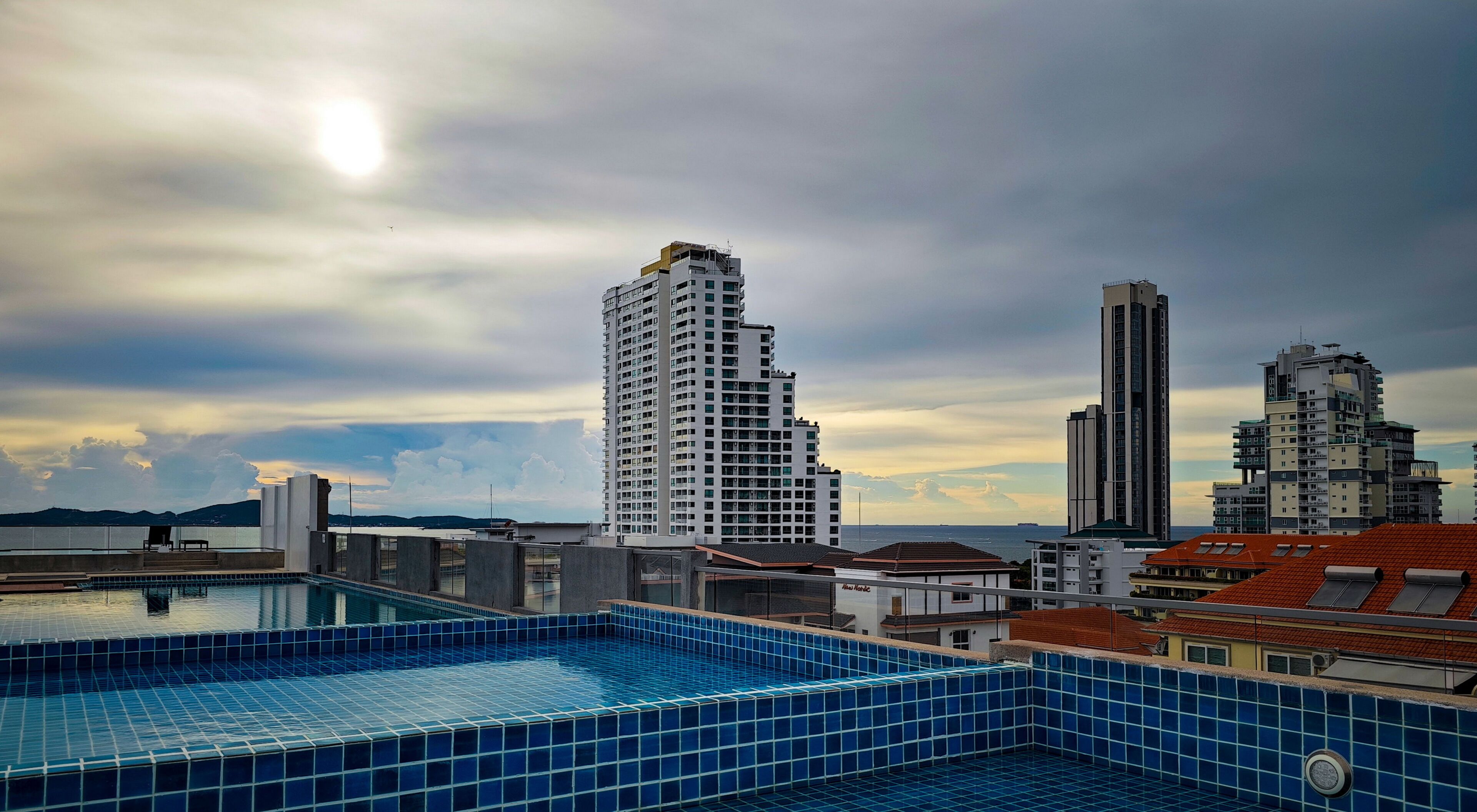 A rooftop pool with a cityscape view, including high-rise buildings and a distant body of water.