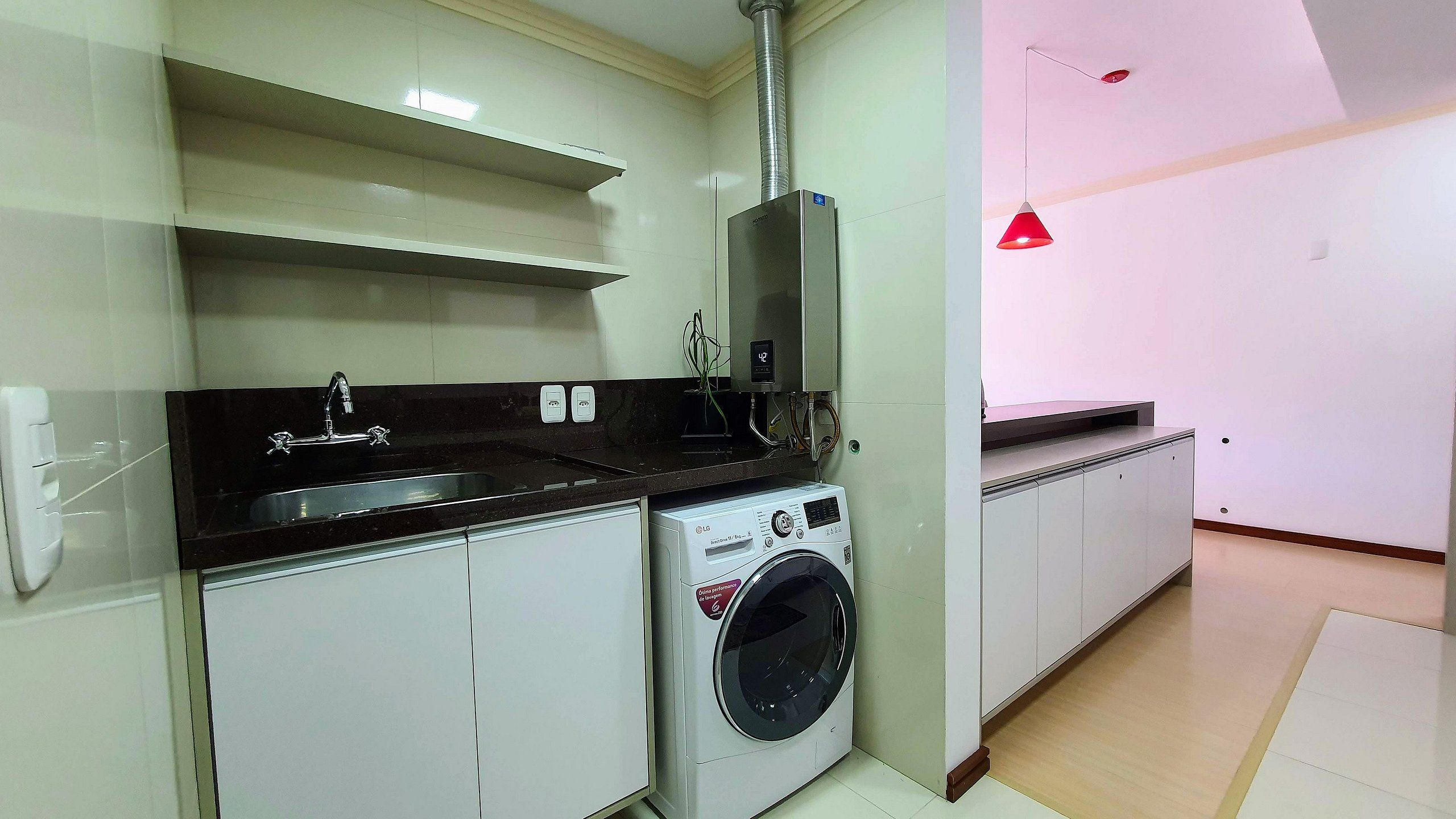Een kleine keuken met een wasmachine, een spoelbak en een rode hanglamp.