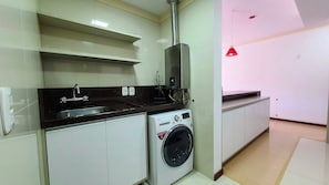 A compact kitchen with a washing machine, a sink, and a red pendant light. - Residencial Dona Virginia (Canela)
