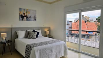 Een slaapkamer met een bed, twee nachtkastjes, een raam met uitzicht op gebouwen en een airconditioning.