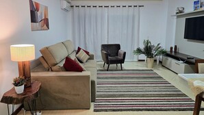 A modern living room with a sofa, armchair, and a TV on a stand. - Residencial Dona Virginia (Canela)