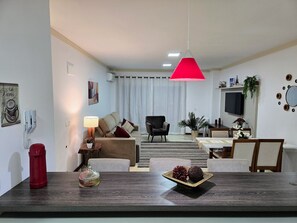 A modern living room with a dining area, featuring a sofa, armchairs, a coffee table, and a TV mounted on the wall. - Residencial Dona Virginia (Canela)