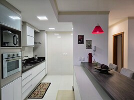 A modern kitchen with white cabinets, a built-in oven, a microwave, and a stove. There is a wooden dining table with a red pendant light above it.
