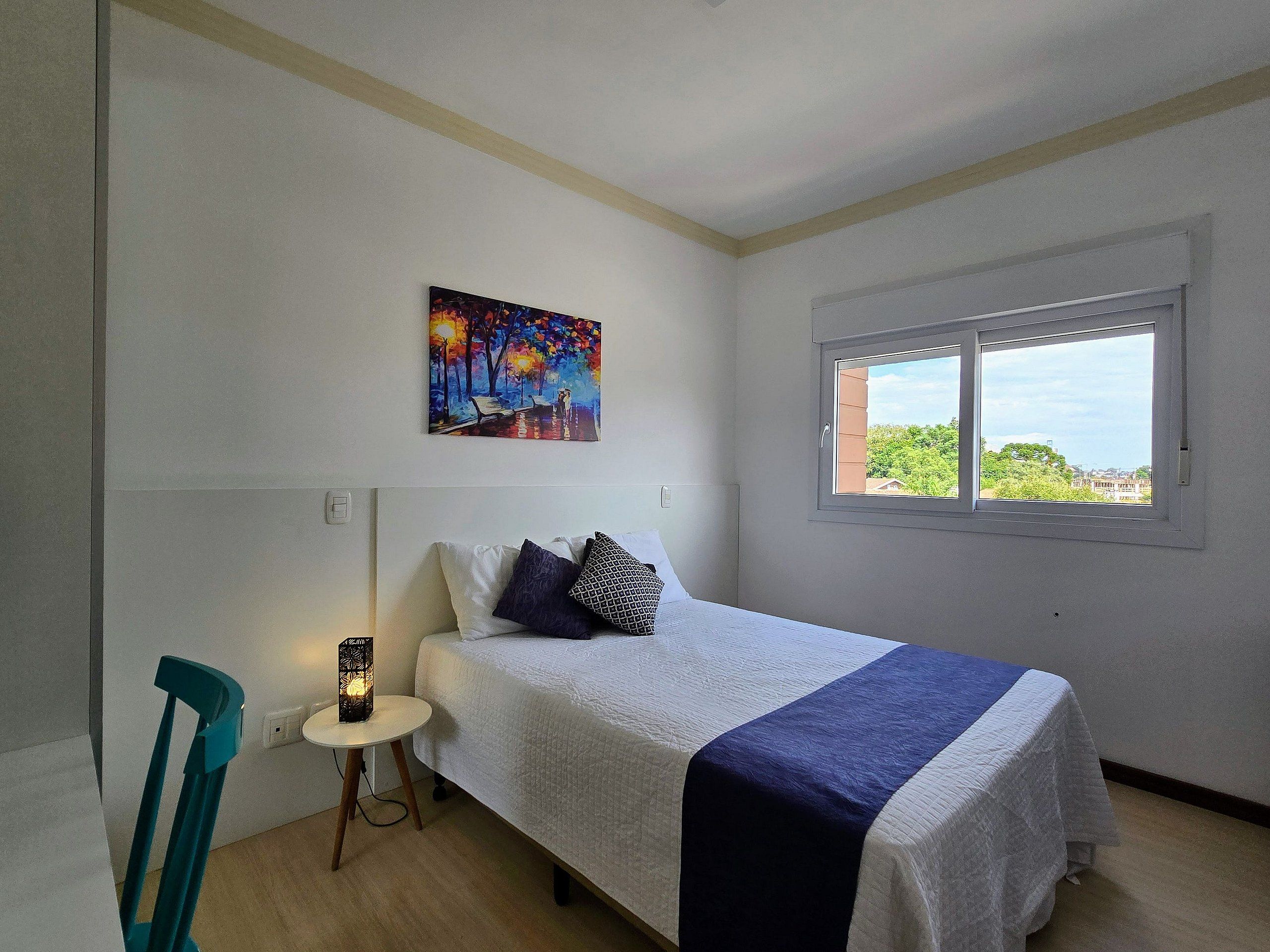 Un dormitorio con cama, un cuadro, una ventana y una silla.