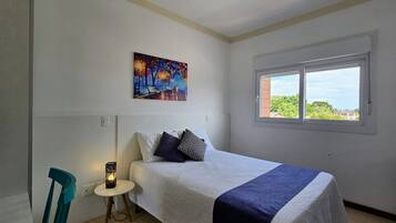 Un dormitorio con cama, un cuadro, una ventana y una silla.