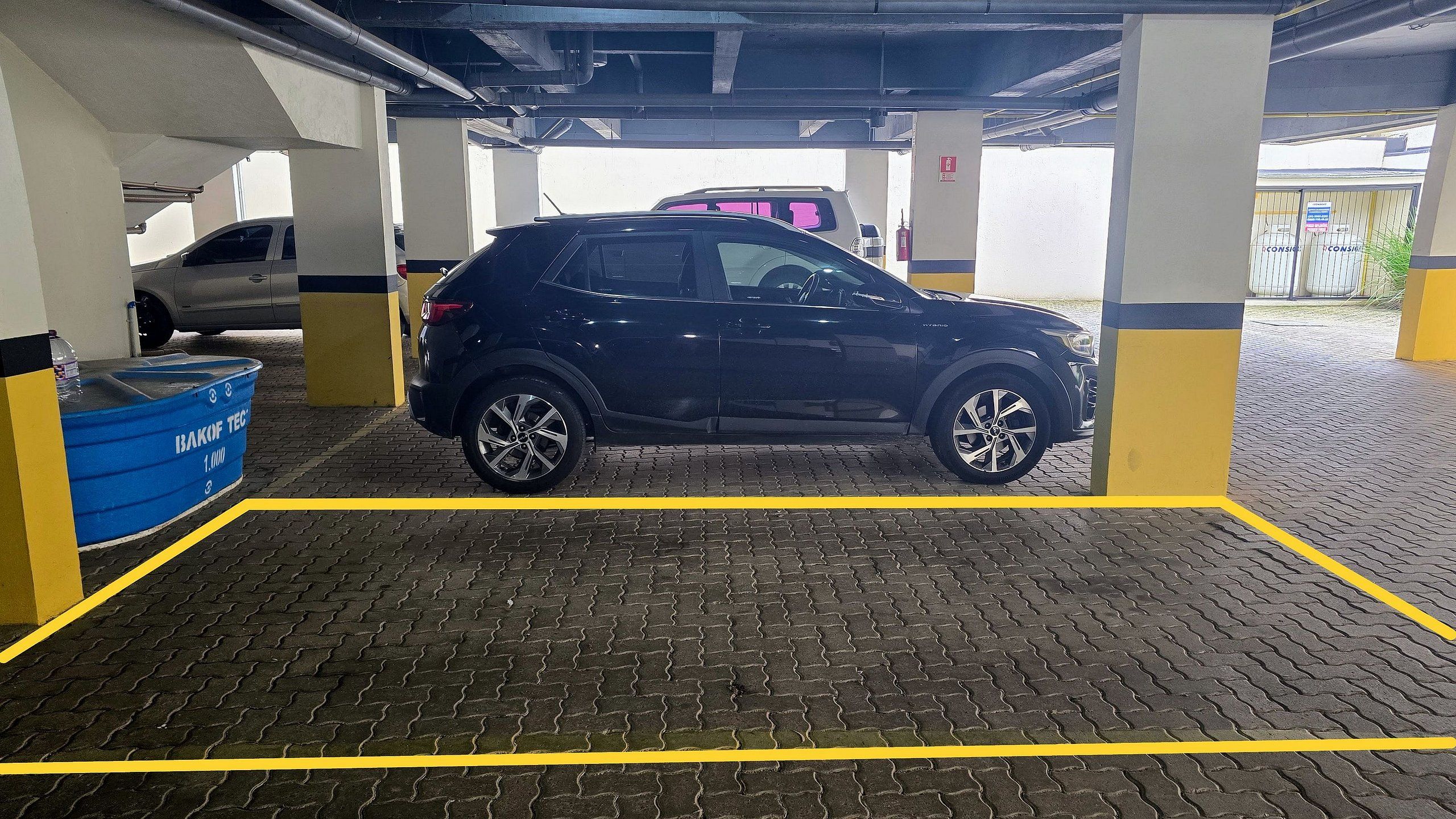 Un estacionamiento con un coche azul aparcado en un espacio delimitado por líneas amarillas.