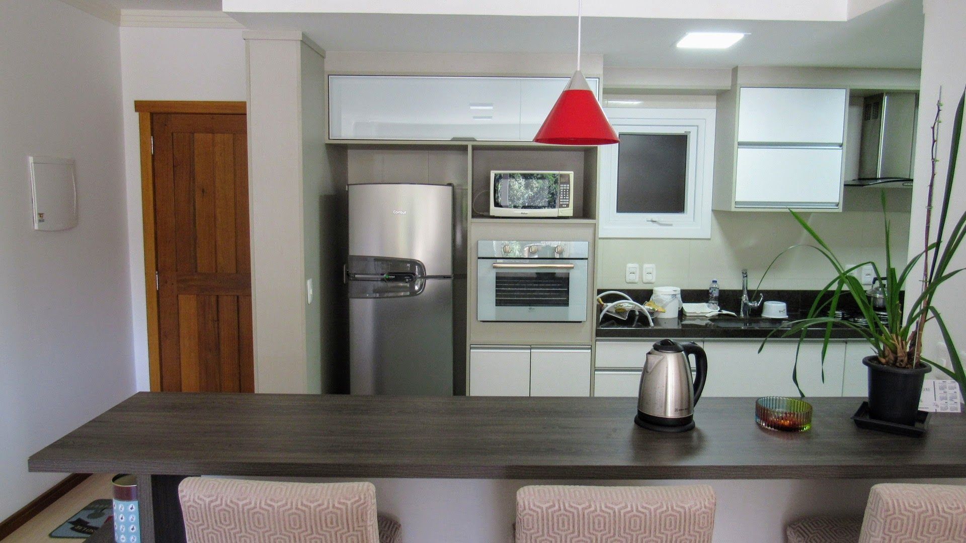 A modern kitchen with a refrigerator, microwave, oven, and a kettle on the counter.