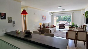A modern living room with a sofa, armchairs, a dining table, and a kitchen area with a counter. - Residencial Dona Virginia (Canela)