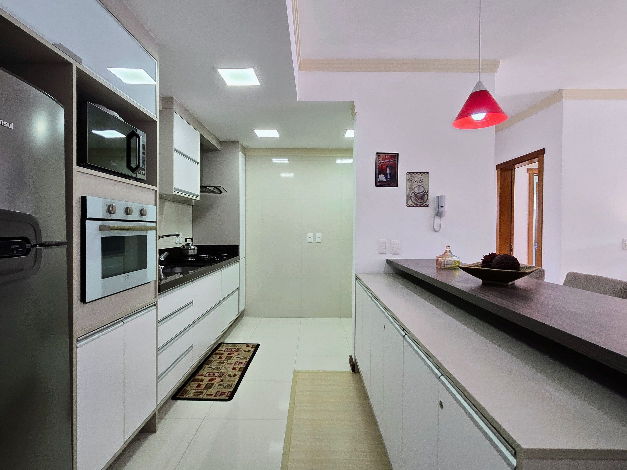 Una cocina moderna con armarios blancos, electrodomésticos de acero inoxidable y una lámpara colgante roja.
