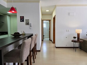 A modern kitchen with a dark countertop, a red hanging light, and a wooden dining area with patterned chairs. - Residencial Dona Virginia (Canela)