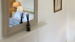Un dormitorio con un espejo grande y ornamentado, una cama con ropa de cama blanca, una mesita de noche con una lámpara y una obra de arte enmarcada en la pared.