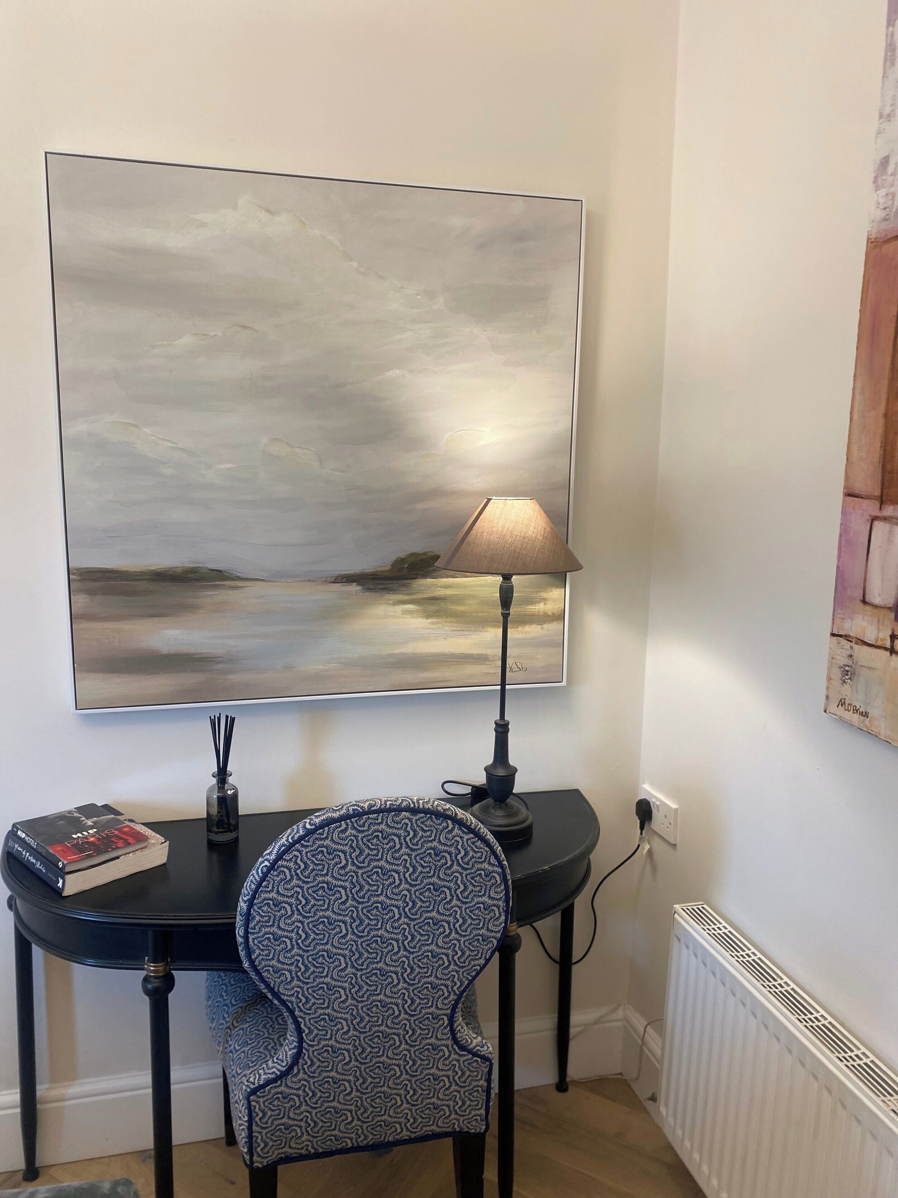 A desk with a lamp, a chair, a painting, and a radiator.