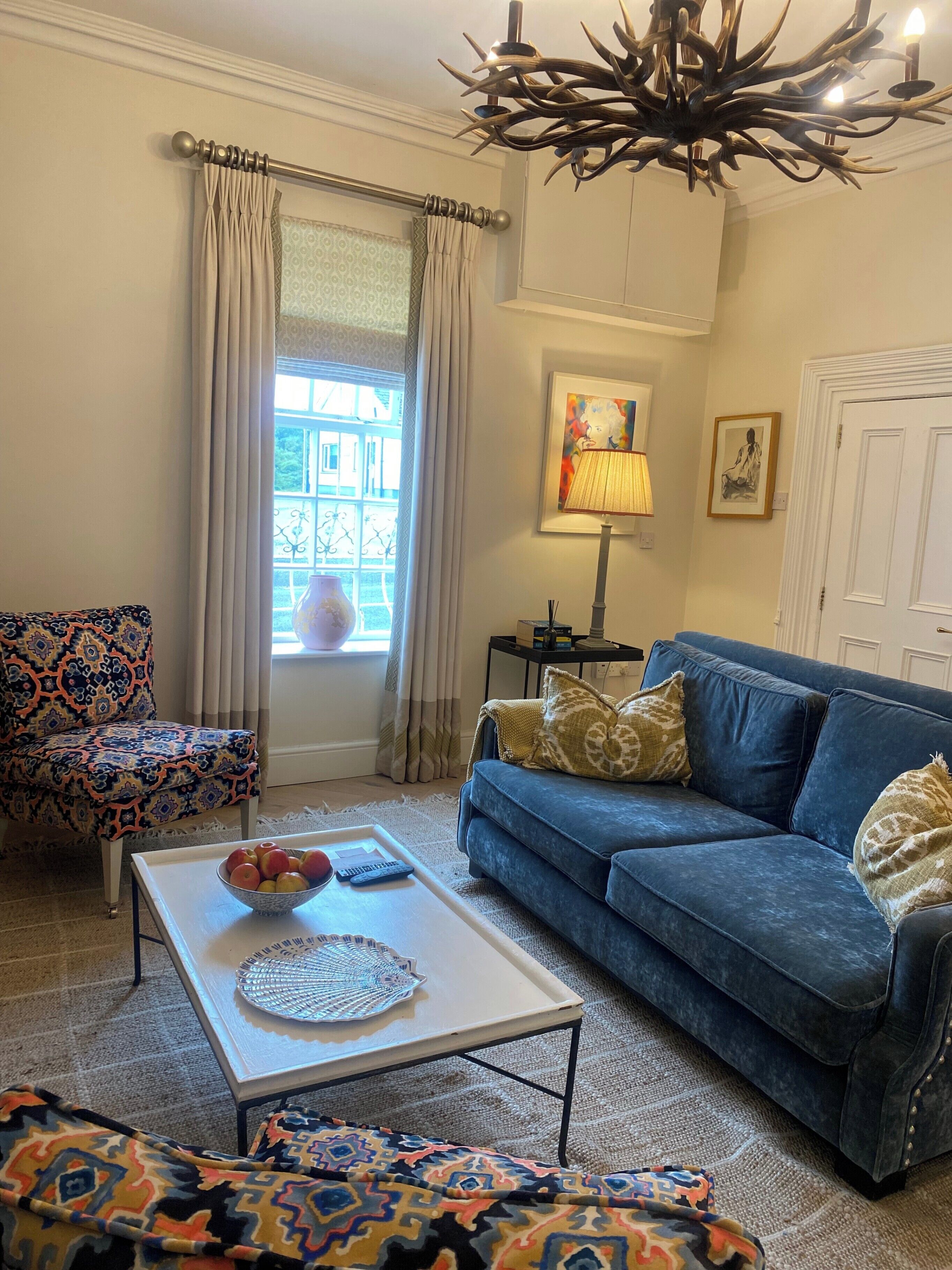 Un salon avec un canapé bleu, un fauteuil à motifs et une table basse sur laquelle se trouve un saladier rempli de fruits.