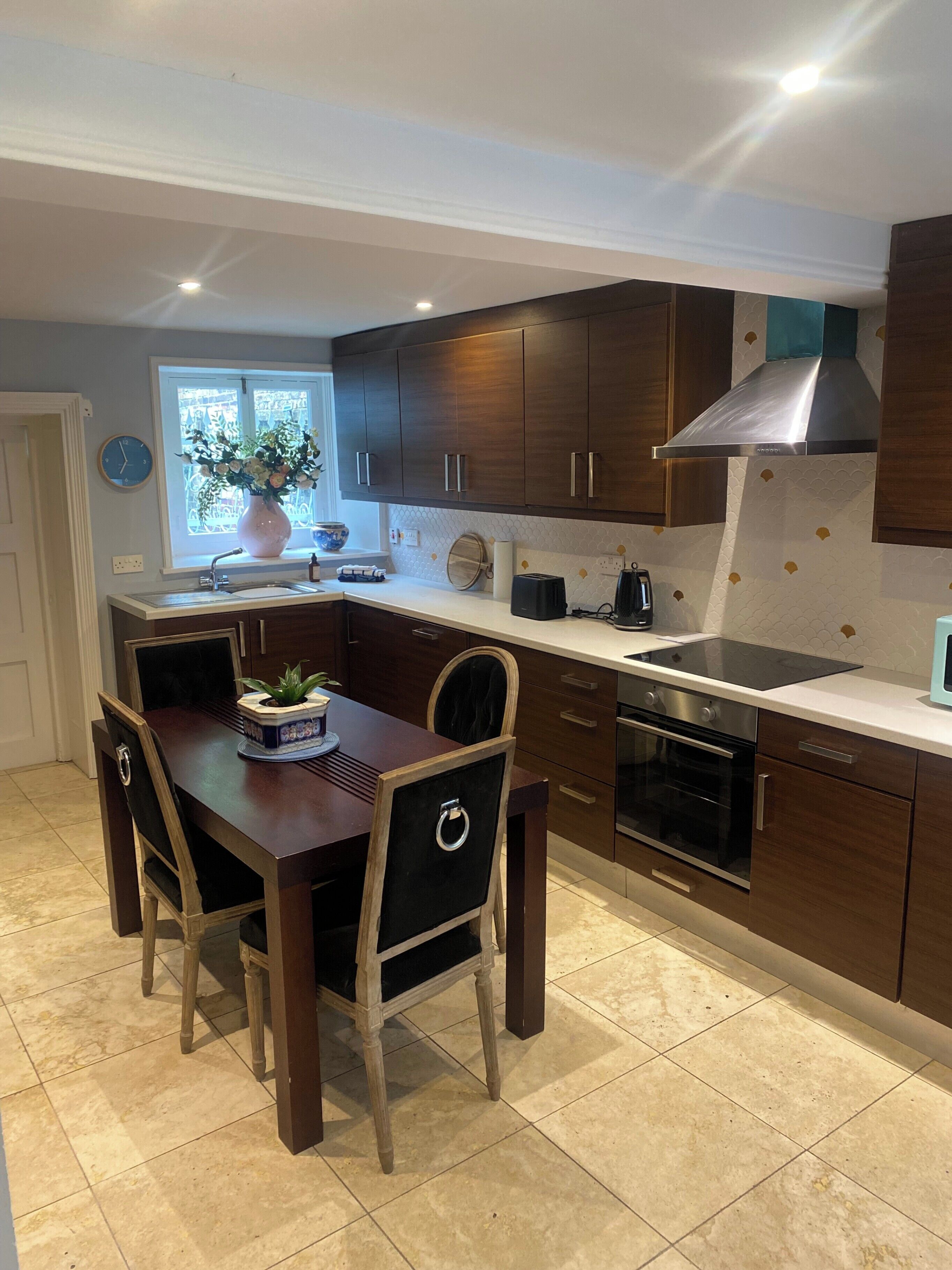 A modern kitchen with wooden cabinets, a stainless steel range hood, a built-in oven, and a dining area with a wooden table and chairs.