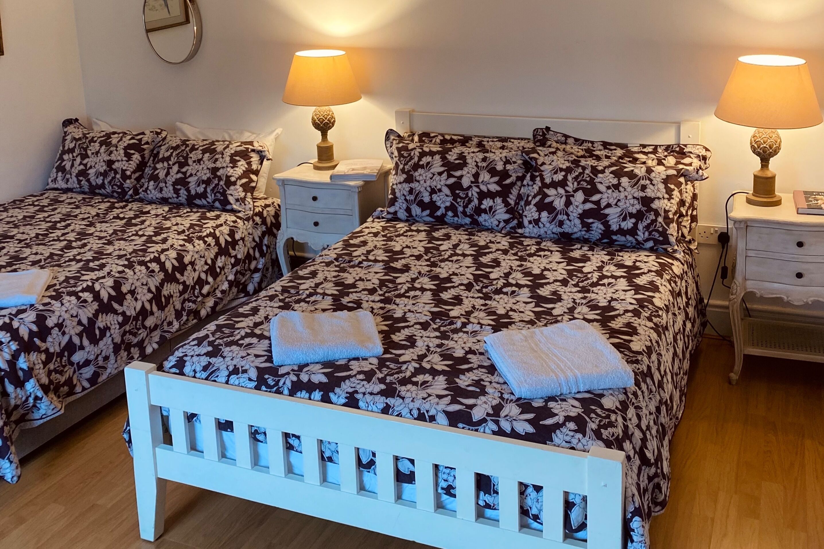 Dos camas individuales con ropa de cama floral, lámparas de noche y un cabecero blanco.