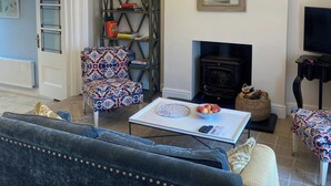 Una sala de estar con una araña, una chimenea, un sillón estampado, un sofá y un televisor.