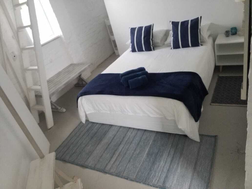 Een slaapkamer met een bed, kussens, een nachtkastje en een klein tapijt.